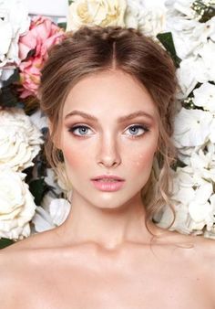 a woman with blue eyes and blonde hair standing in front of white flowered wall