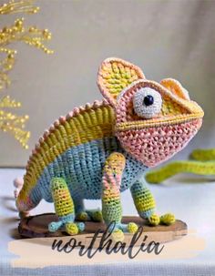 a small crocheted chamelon sitting on top of a piece of wood