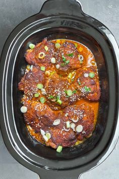 a slow cooker filled with meat covered in sauce and garnished with green onions