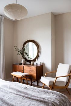 a bedroom with a bed, chair and mirror in it's corner next to a window