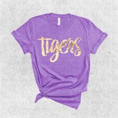 Soft comfy t-shirt and tank with gold foil lettering. Perfect for any tiger events!  T-Shirts are unisex fit and true to size. Tanks are  fitted and true to size. Size up for looser fit. NOTE: When laundering, please do not use fabric softener and wash inside out if possible. Fabric softener and other additives can cause the foil to break down and will likely render the shirt unwearable. Please reach out to me with any questions. Gold Short Sleeve Top With Screen Print, Gold Crew Neck Top With Screen Print, Gold Short Sleeve Top With Text Print, Gold Crew Neck Top With Text Print, Gold Graphic Tee With Screen Print, Tigers Tshirt Ideas, Gold Graphic Tee With Letter Print, Casual Gold T-shirt With Screen Print, Gold Screen Print Graphic Tee Tops