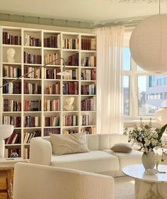 a living room filled with lots of white furniture and bookshelves next to a window