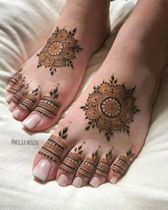 two feet with henna tattoos on them, one is decorated in gold and the other has