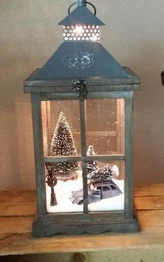 a small lantern is lit up with christmas trees in the window and snow on the ground