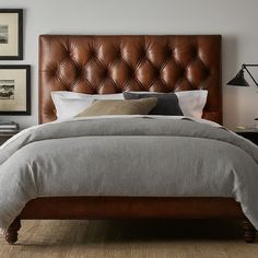 a bed with a brown leather headboard in a bedroom next to pictures on the wall