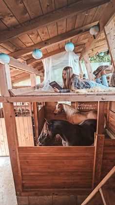 a woman sitting on top of a wooden structure next to two cows in a pen