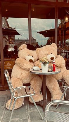 two large teddy bears sitting at a table with a cup of coffee in front of them