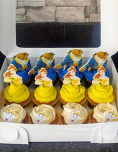 cupcakes with yellow frosting and disney characters on them in a white box