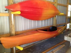 two kayaks are hanging from the wall in a garage, one is orange and the other is red