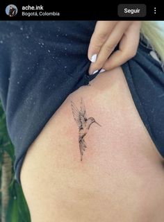 a small hummingbird tattoo on the back of a woman's stomach is shown