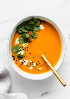 a white bowl filled with carrot soup and garnished with herbs