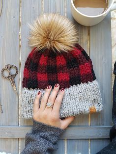 a woman's hand on top of a knitted hat next to a cup of coffee