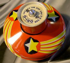 an old fashioned red and yellow tin can with stars on the side, sitting on a gray cloth