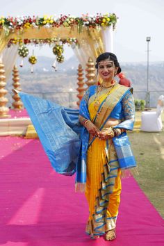 a woman dressed in yellow and blue walking down a pink carpeted aisle with flowers on it