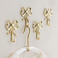 three gold coat hooks hang on a white wall next to a white shirt with bows