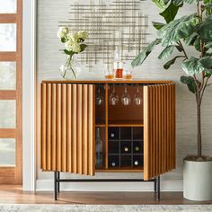 a wooden cabinet with wine glasses and bottles in it next to a potted plant