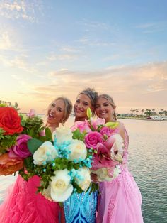 three beautiful women standing next to each other near the water with flowers in their hands