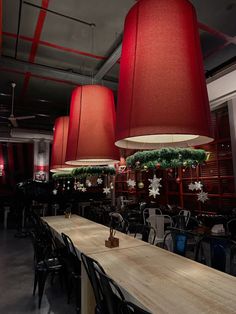 several red lamps hanging from the ceiling in a room with long tables and black chairs