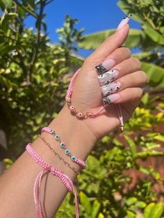 a woman's hand with bracelets and rings on her wrist in front of some trees