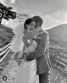 a bride and groom hugging each other in front of a fence with mountains behind them