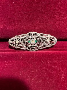 Excellent representation of a classic Victorian Filigree pin in Sterling Silver with white and green synthetic accent stones, which mimic diamond and emerald brooches from that period. This piece from our Estate Collection is in excellent condition. The pin stem is held in place via a safety clasp. This piece may be worn horizontally, vertically, or even on the diagonal, as you wish. It could even be worn vertically on a chain, if desired. While this piece is vintage, it is not technically an antique; although only you need to know as this will easily pass as a well-preserved antique. Ornate Diamond Brooches With Intricate Design, Ornate Diamond Brooch With Intricate Design, Victorian Diamond Filigree Brooches, Green Diamond Wedding Brooches, Ornate Diamond Brooches For Formal Occasions, Ornate Diamond Brooch For Formal Wear, Diamond Filigree Brooches As Gift, Ornate Diamond Brooch For Formal Occasions, Formal Silver Jeweled Brooches