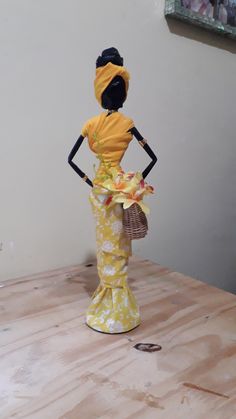 a doll is standing on a table with a basket in her hand and wearing a yellow dress