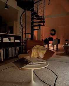 a living room with a spiral staircase next to a table and books on the floor