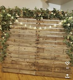 a wooden wall with flowers and greenery on the top is decorated with string lights