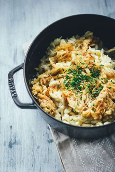 a skillet filled with chicken and rice on top of a wooden table next to a napkin