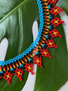 a colorful beaded necklace sitting on top of a green leaf next to a plant