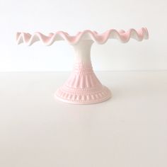 a small pink cake stand on a white table with no one around it and the base is covered in icing