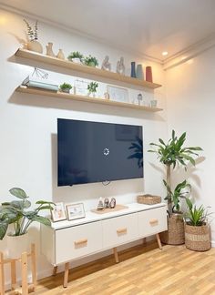 a flat screen tv sitting on top of a wooden shelf next to potted plants