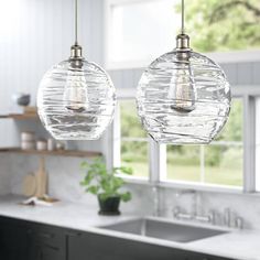 two clear glass globe pendant lights hanging over a kitchen counter with sink and window in the background