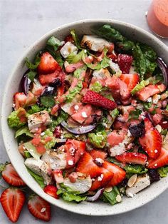 a salad with strawberries and dressing in a white bowl next to an orange juice