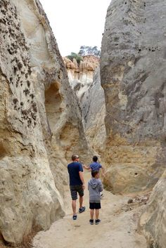 two men are standing in the middle of a narrow path between large rocks and boulders