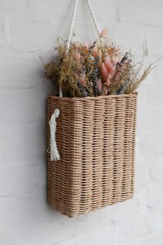 a wicker basket hanging on a white brick wall with dried flowers and foliage in it