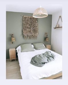 a white bed sitting under a hanging light next to a wooden dresser and lamp shade