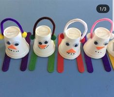 four plastic snowman cups and spoons lined up on a blue surface with colorful handles