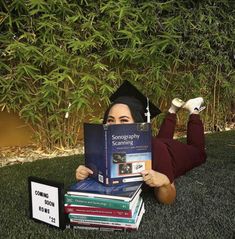 a woman laying on the grass with books in her hands and a sign reading something