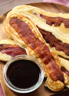 two hotdogs with bacon and ketchup sit on a plate next to a jar of sauce