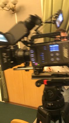 a man sitting in front of a camera on top of a tripod next to a tv monitor