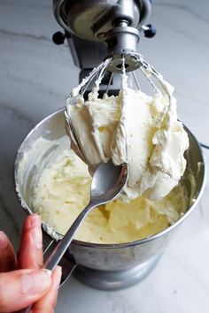 a hand holding a whisk over a metal mixing bowl filled with whipped cream