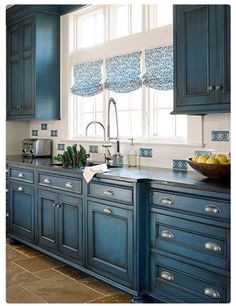 a kitchen with blue cabinets and tile flooring, along with a bowl of fruit on the counter