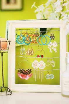 a white frame holds several pairs of earrings and bracelets in front of a vase with flowers