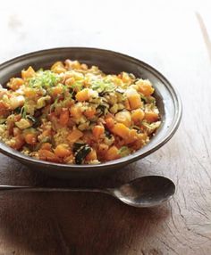 a bowl filled with food sitting on top of a wooden table next to a spoon