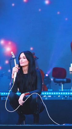 a woman sitting on the ground with a microphone in her hand and lights behind her