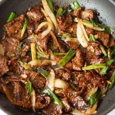 beef and onions stir fry in a wok with green onions on the side, ready to be eaten