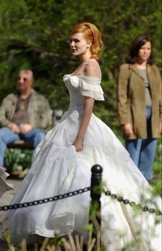 a woman in a white wedding dress is walking down the street with people behind her