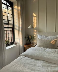 a bed with white linens and pillows in front of a window, next to a lamp