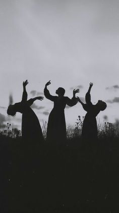 three people standing on top of a grass covered hill with their arms in the air